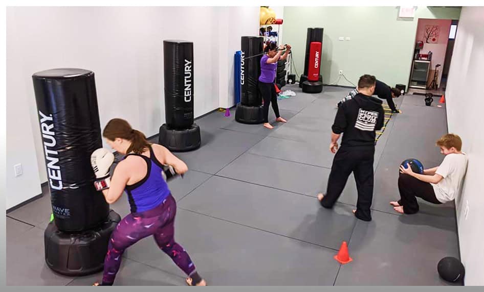 Women practicing kickboxing with punching bags at Johnny Karate NYC gym.