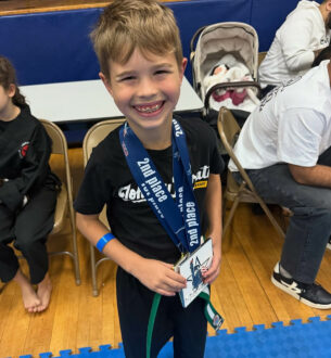 Young boy smiling with medal after karate competition.