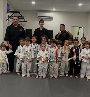Group of children in martial arts uniforms with instructors at Johnny Karate NYC.