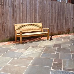 Bench along a wooden fence with stone paving.