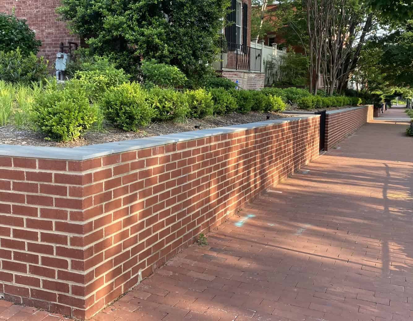 Brick wall with landscaped garden and sidewalk in a historic neighborhood.