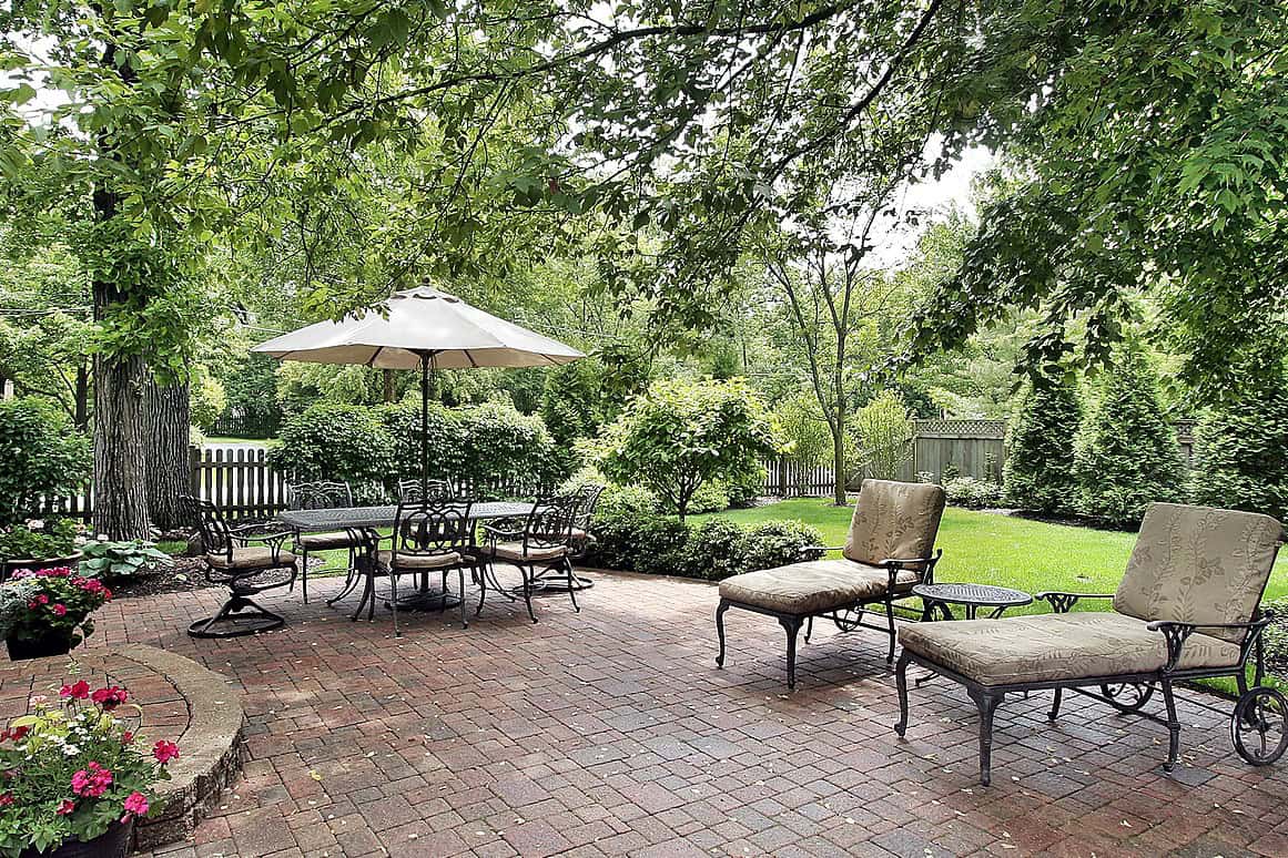 Outdoor patio with brick flooring, garden furniture, and lush greenery.