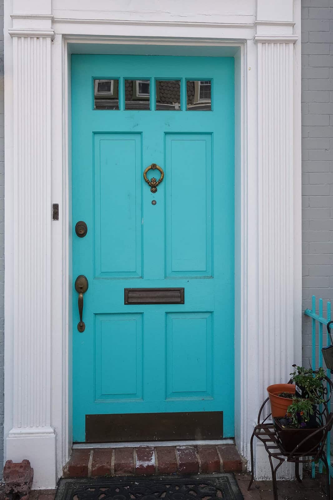 Bright turquoise front door with decorative hardware and transom windows.