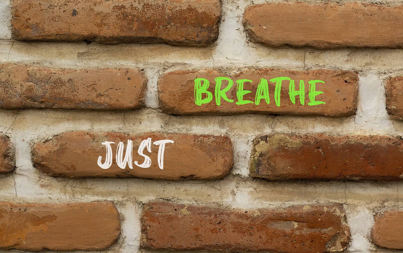 Close-up of brick wall with "BREATHE" and "JUST" graffiti in green and white.