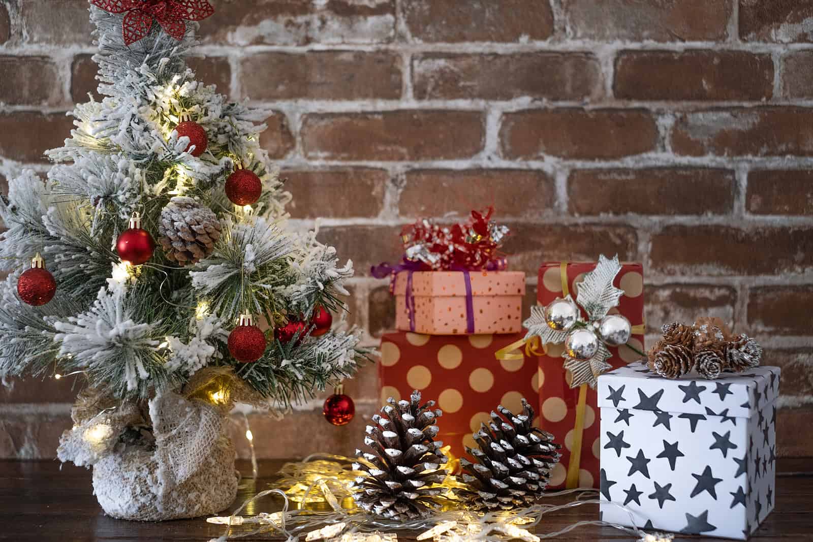 Decorative Christmas scene with a small decorated tree and wrapped gifts against a brick wall.