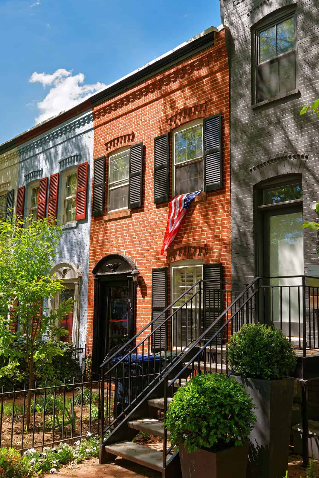 Historic brick townhouse with black shutters and American flag, showcasing masonry work.