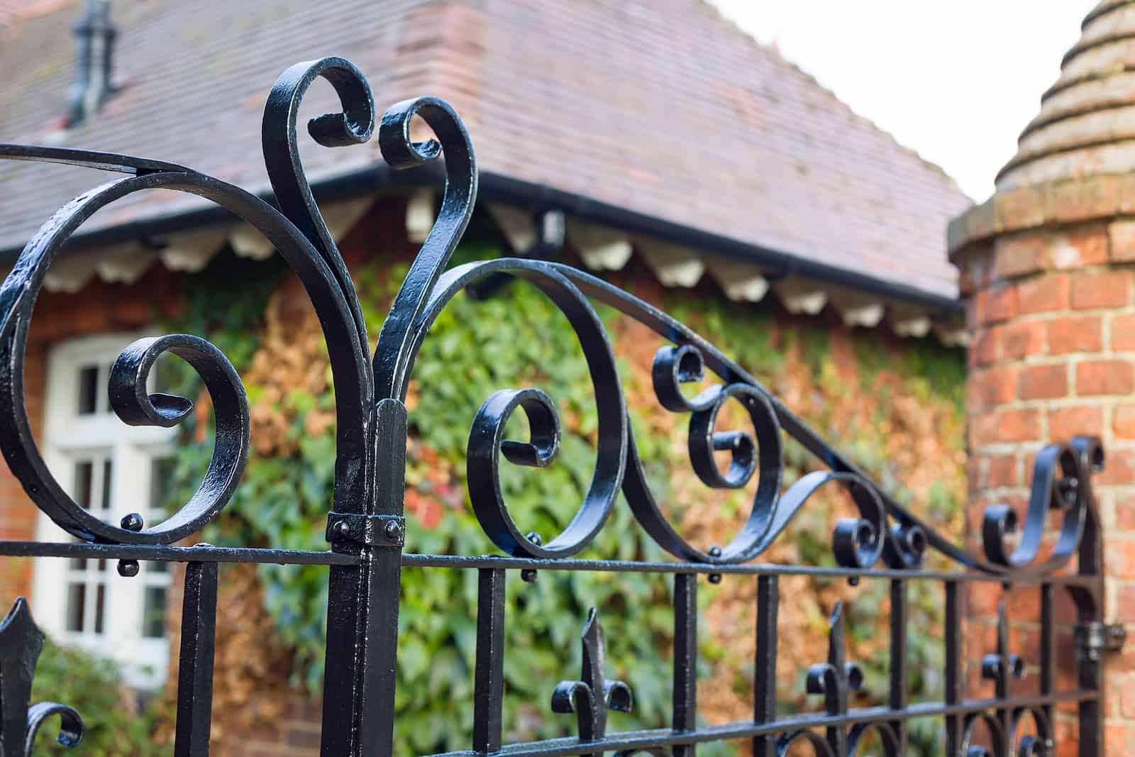 Close-up of decorative wrought iron fence with brick house in background.