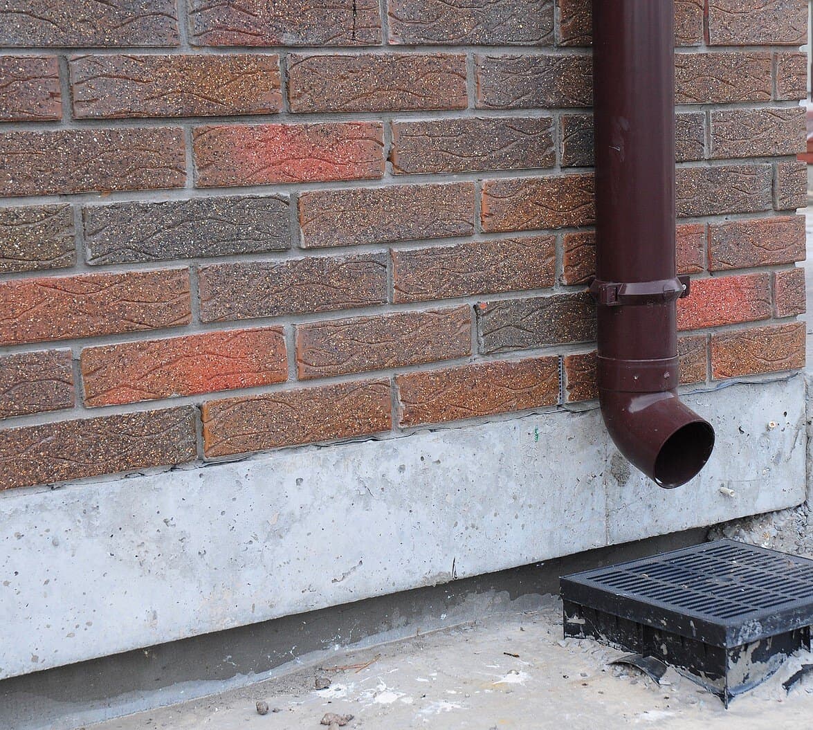 Close-up of brick wall with brown drainpipe and concrete foundation.
