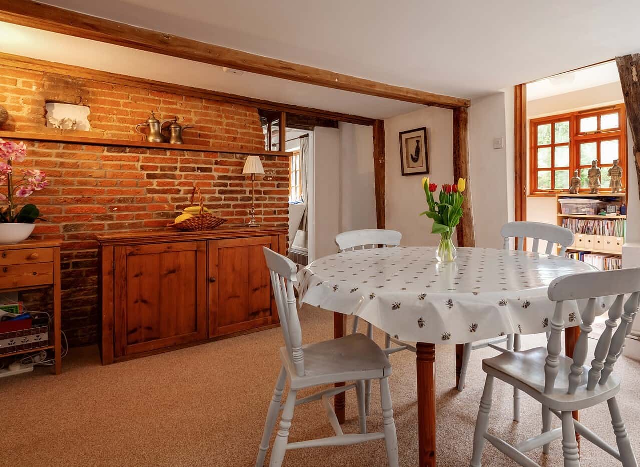 Charming dining area with exposed brick walls, wooden beams, and a round table with a vase of tulips.