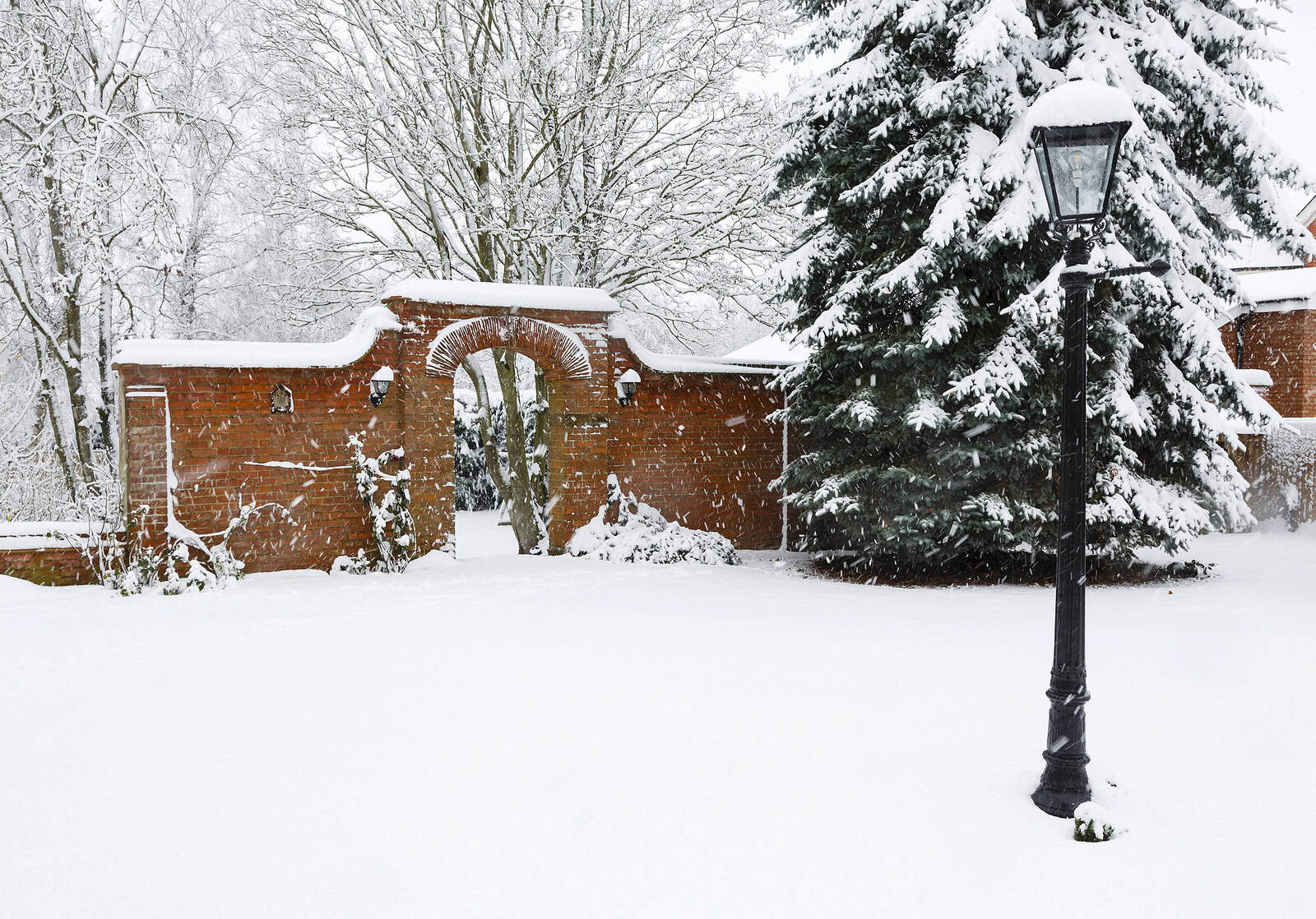 Historic brick wall with archway and snow-covered trees in winter.