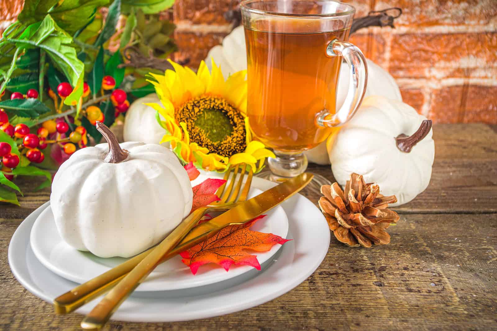 Beautiful autumn-themed scene with white pumpkins, sunflower, pine cone, and a cup of tea on a rusti.