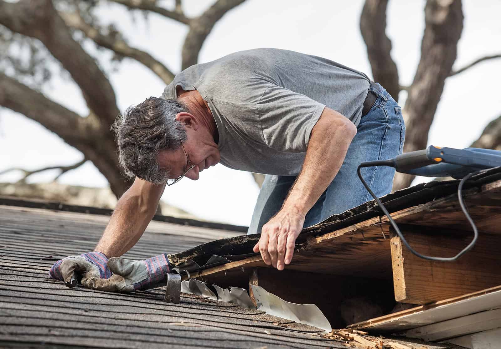 Man repairing roof with tools on historic masonry building.