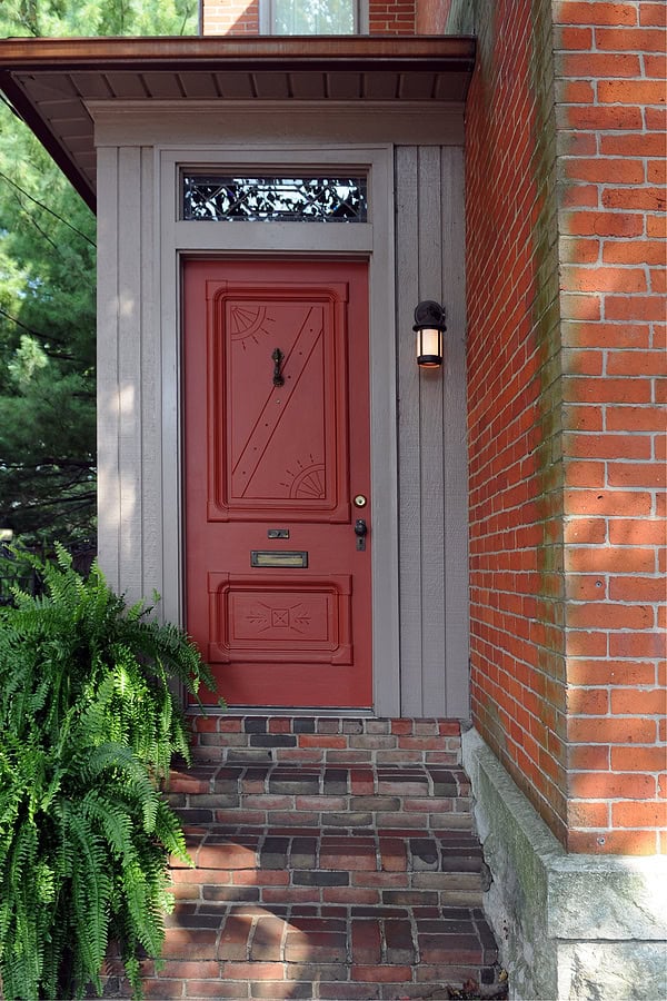 Elegant red front door with decorative details and brick pathway.