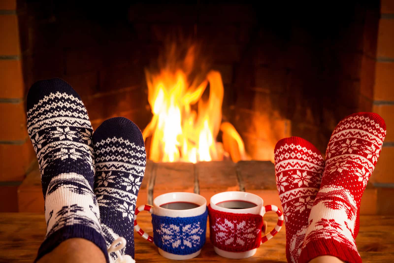 Cozy fireplace scene with warm socks and festive mugs of hot drinks.