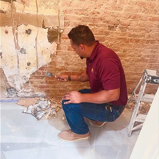 A historic masonry worker performing masonry restoration on a basement wall.