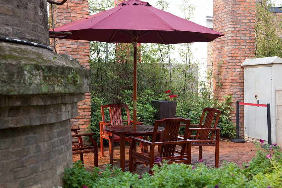 Outdoor patio with wooden table, chairs, and large umbrella in a historic brick setting.