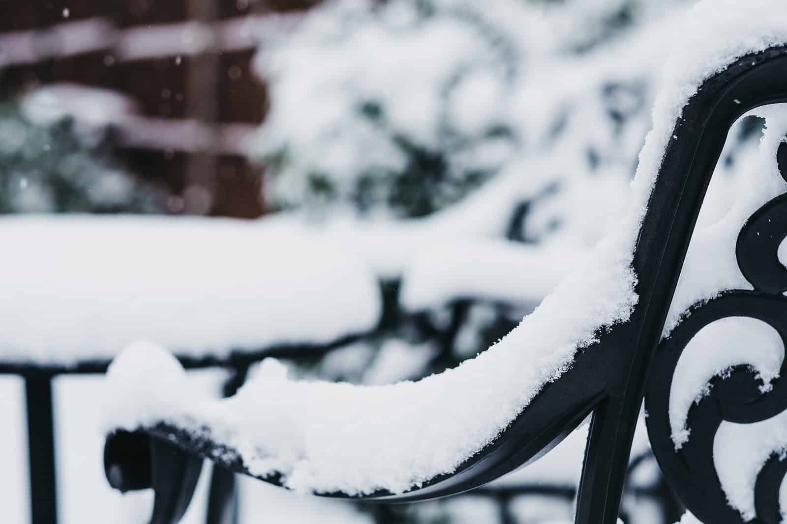 Snow-covered wrought iron bench in a winter scene.