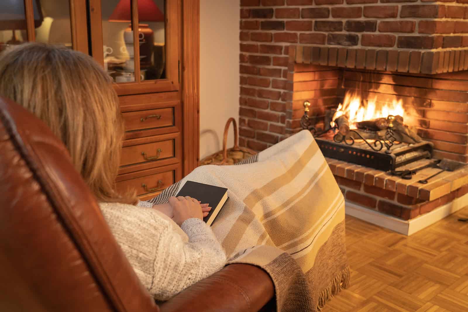 Close-up of a woman relaxing by a cozy fireplace with brickwork.
