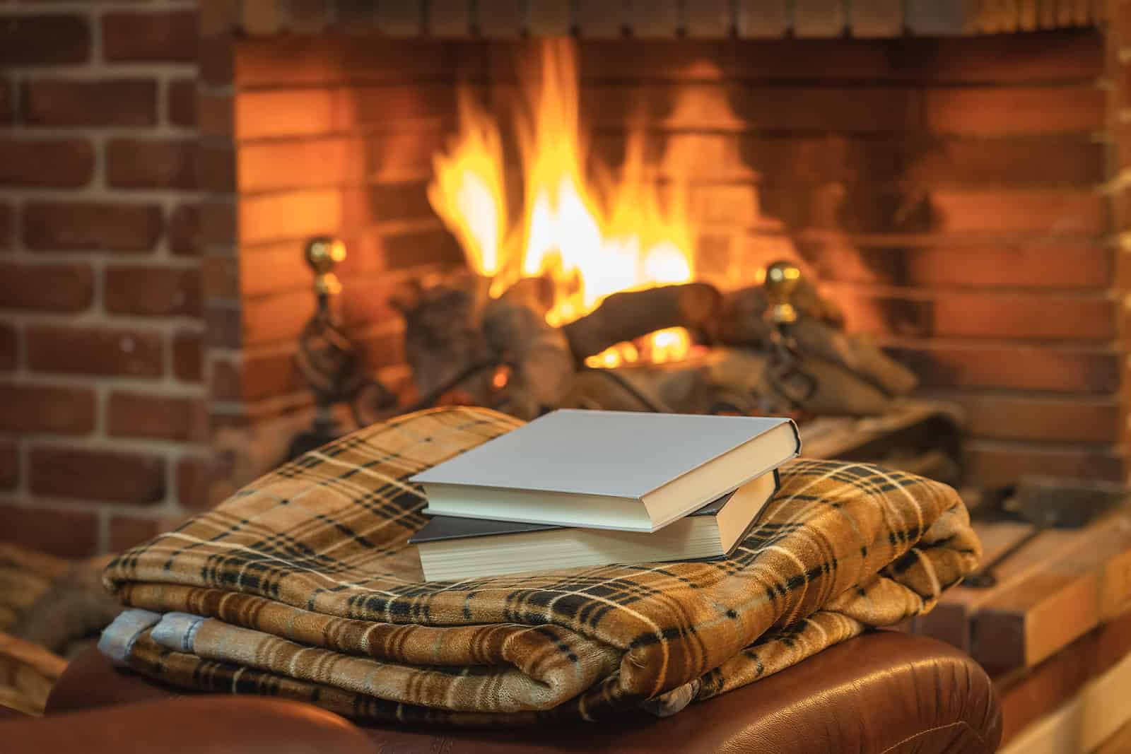 Cozy fireplace with a stack of books and a plaid blanket in front of a brick hearth.