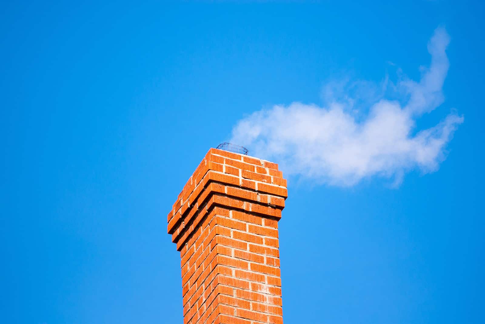 Close-up of a brick chimney with detailed masonry work against a blue sky.