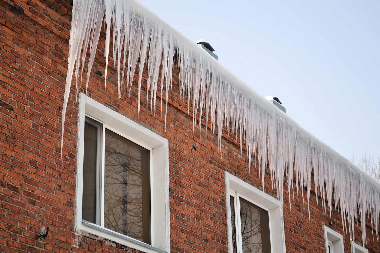 Close-up of brick building with icicles hanging from roof edge, showcasing historic masonry work.