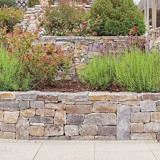 A multiple layer stone retaining wall with foliage and plants.