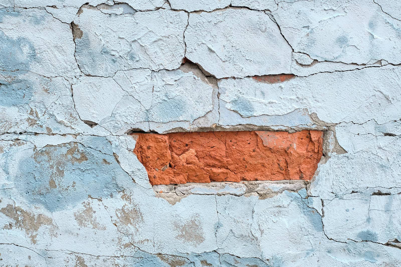 Close-up of deteriorated brick wall with peeling paint and damaged mortar.