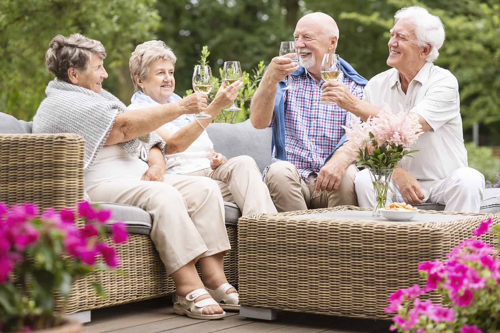 Older adults enjoying drinks outdoors on a patio with lush greenery in the background.