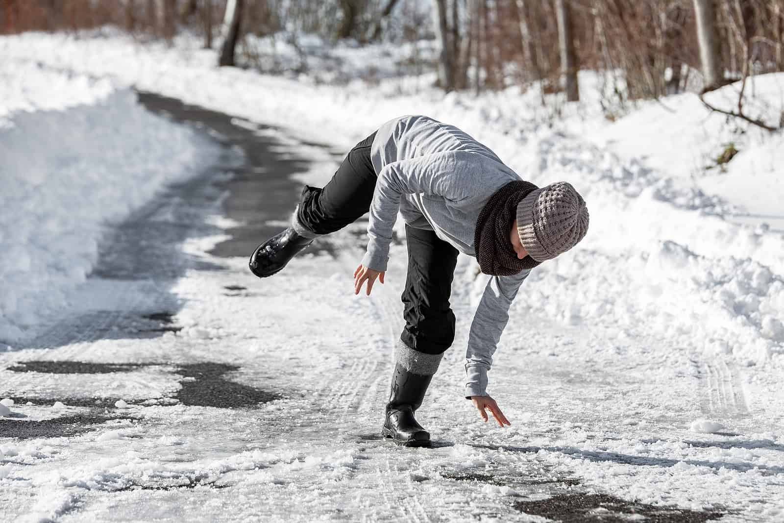 A person slipping on icy snow-covered road during winter, demonstrating the importance of proper mas.