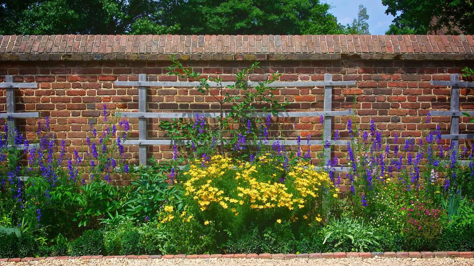 A detailed view of a brick wall with a trellis and colorful flower garden in front, showcasing histo.