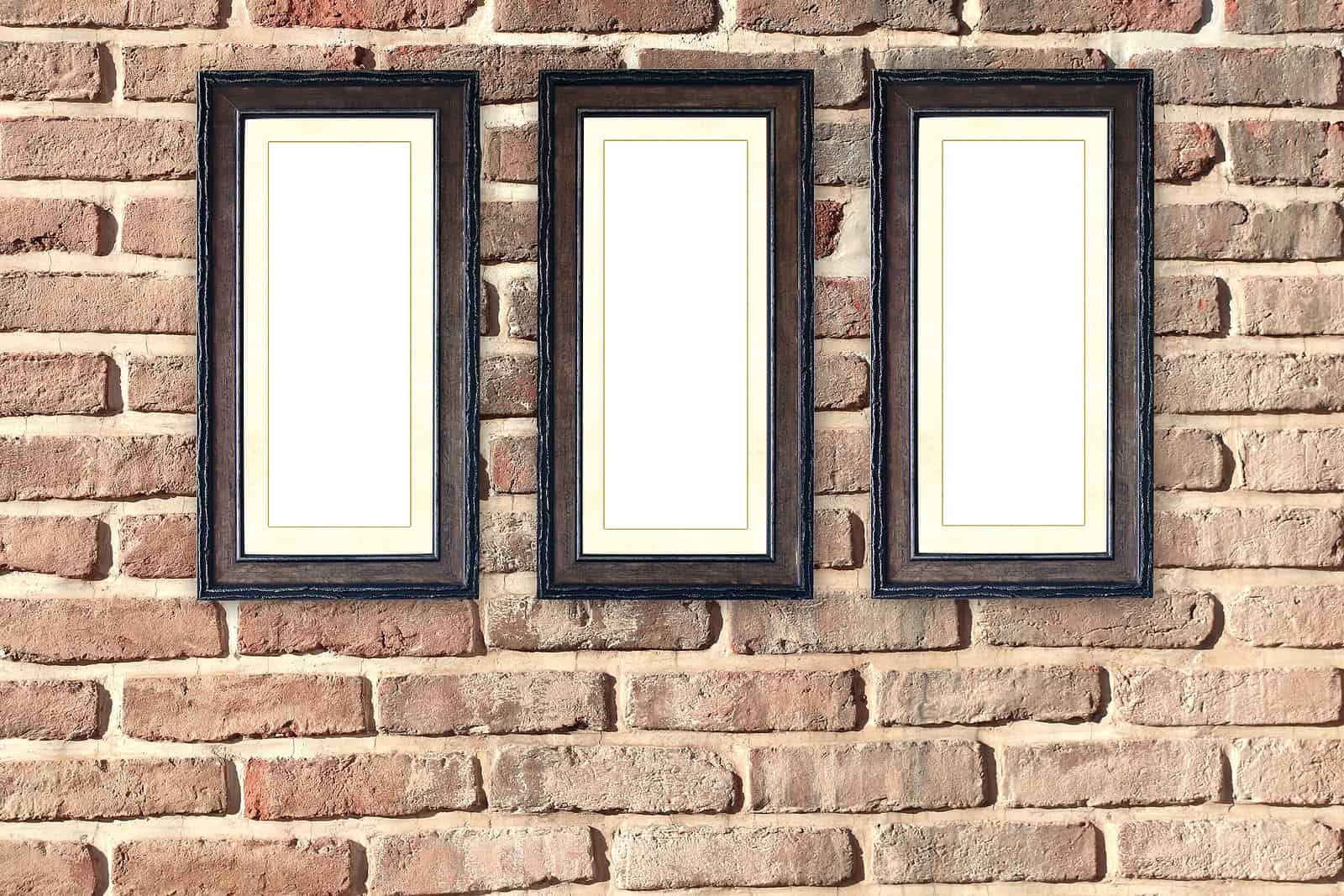 Three framed empty picture frames mounted on a brick wall.