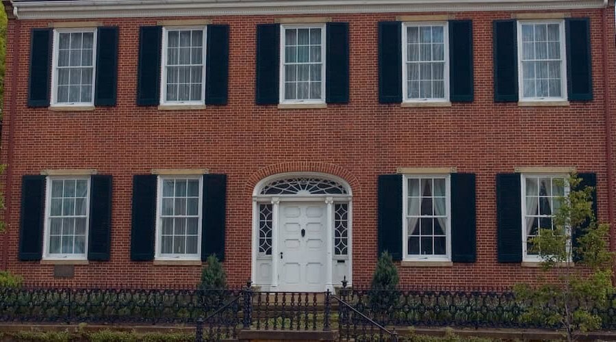 Historic brick building with white door and black shutters, showcasing masonry work.
