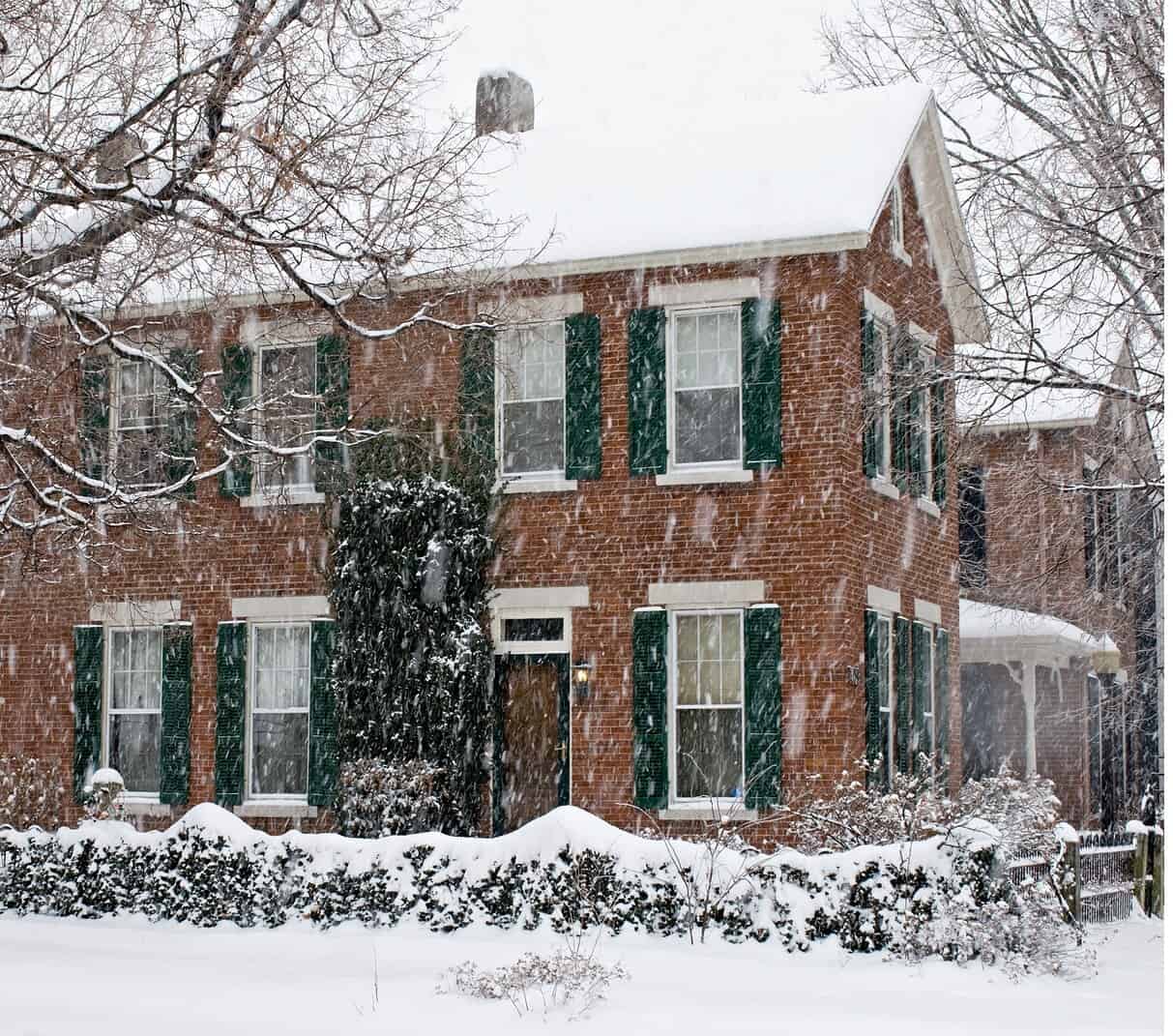Brick house covered in snow with green shutters and historic masonry details.