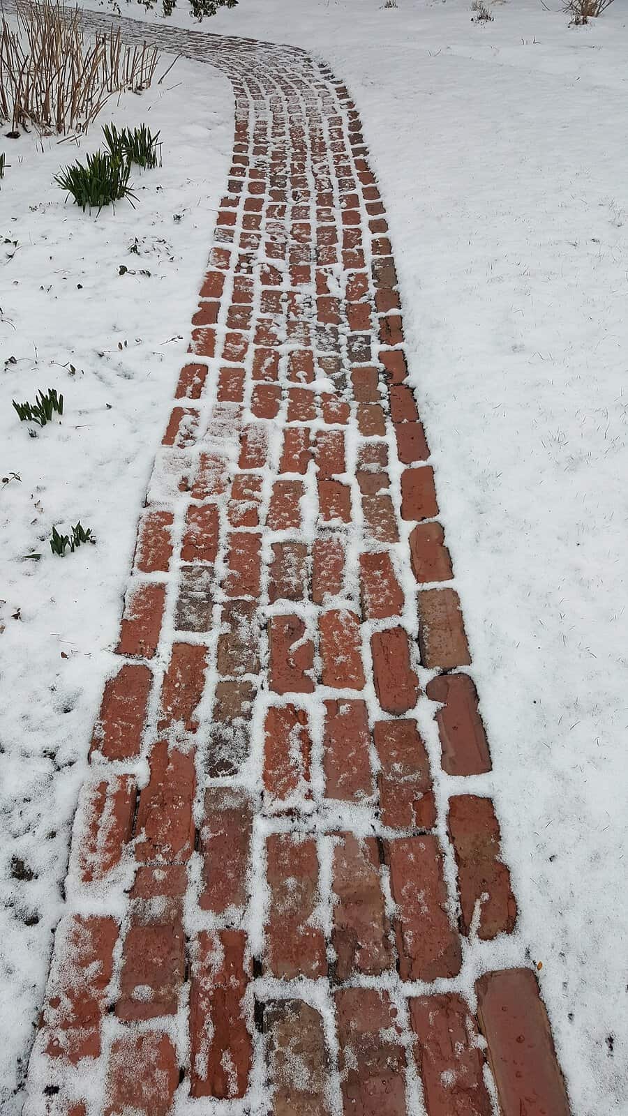 A close-up of a historic brick pathway covered with snow, showcasing detailed masonry work and craft.