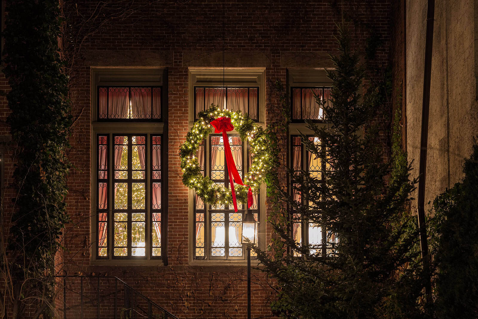 Decorative holiday wreath hanging in front of historic brick building windows.