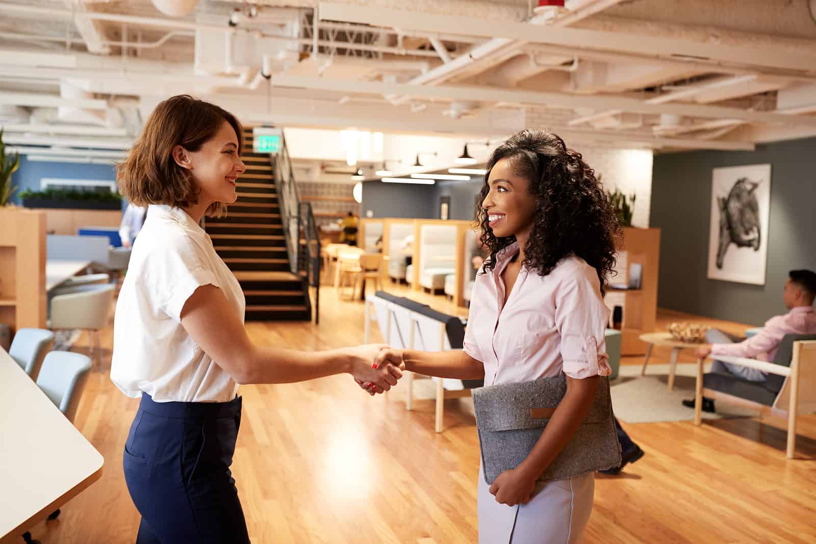 Handshake between two women in a modern office setting.