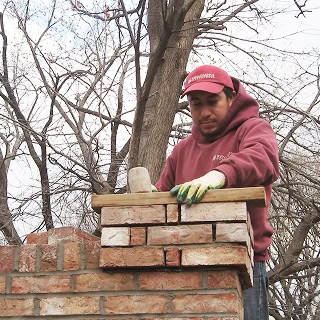 Worker performing tuckpointing on historic brick wall.