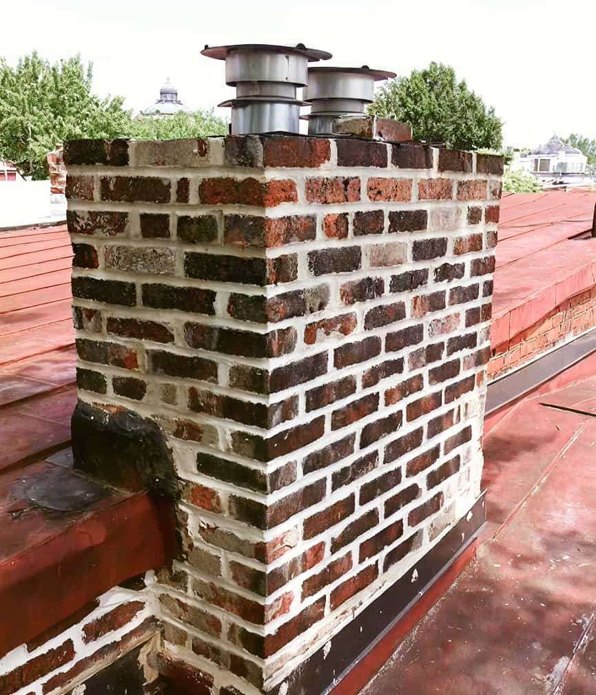 Chimney with historic brickwork and modern venting system on a rooftop.