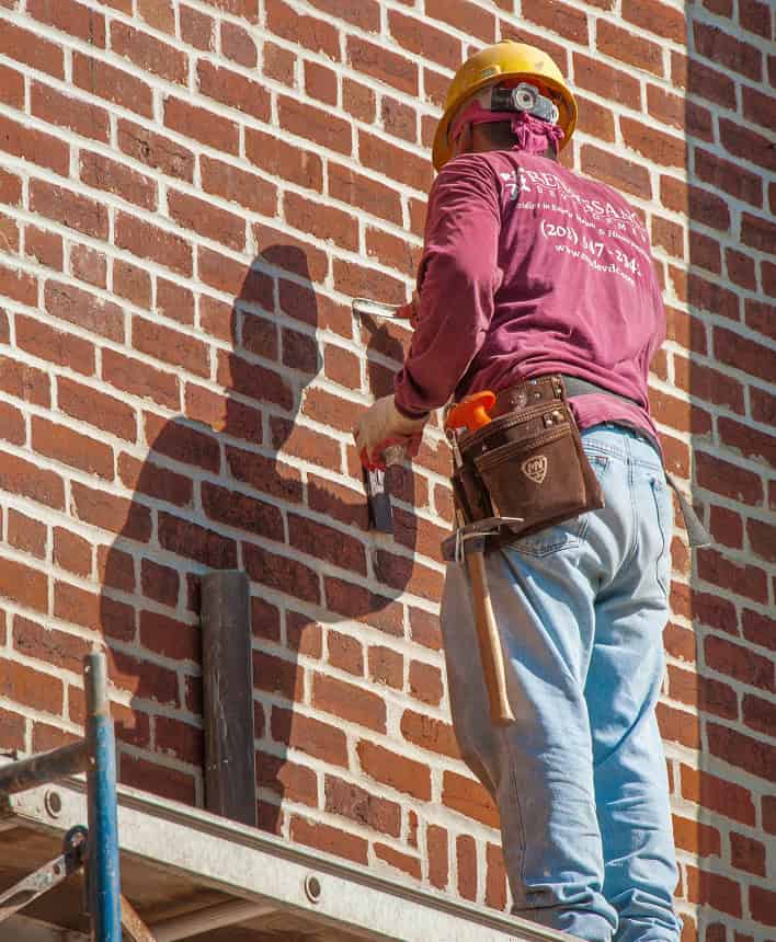 Worker repairing historic brick masonry wall with shadow cast on surface.