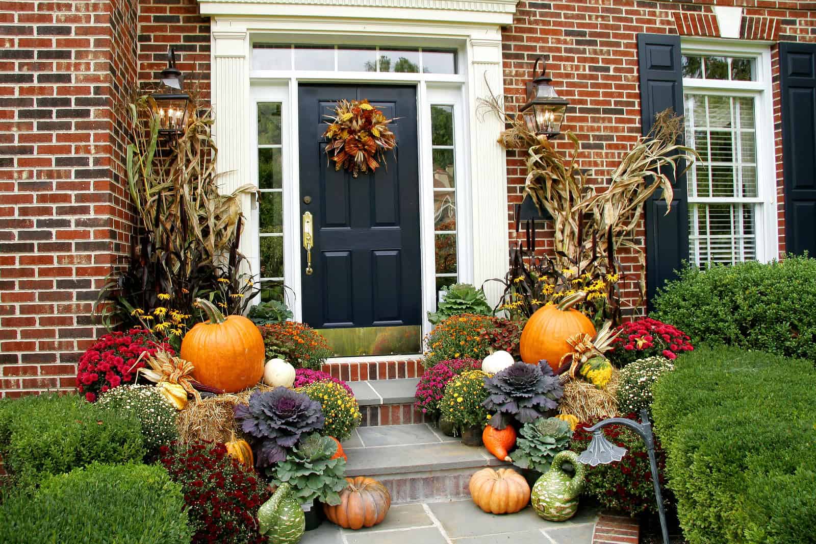 A festive fall front porch decorated with pumpkins, gourds, mums, and autumn foliage, creating a war.