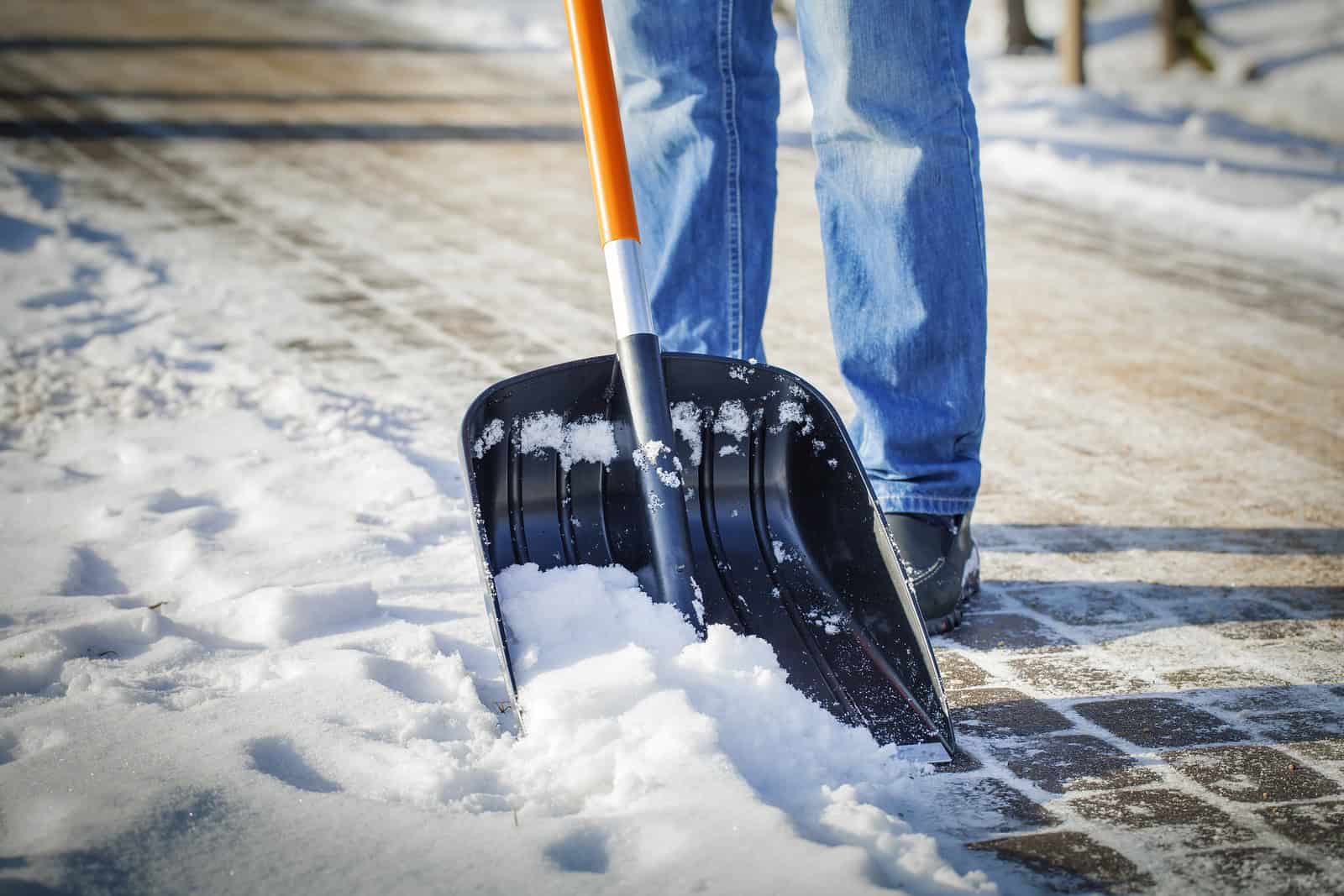 Person shoveling snow from a brick sidewalk with a snow shovel in winter.