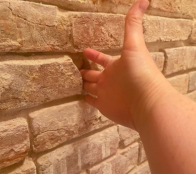 Close-up of hand pointing at historic brick masonry wall.