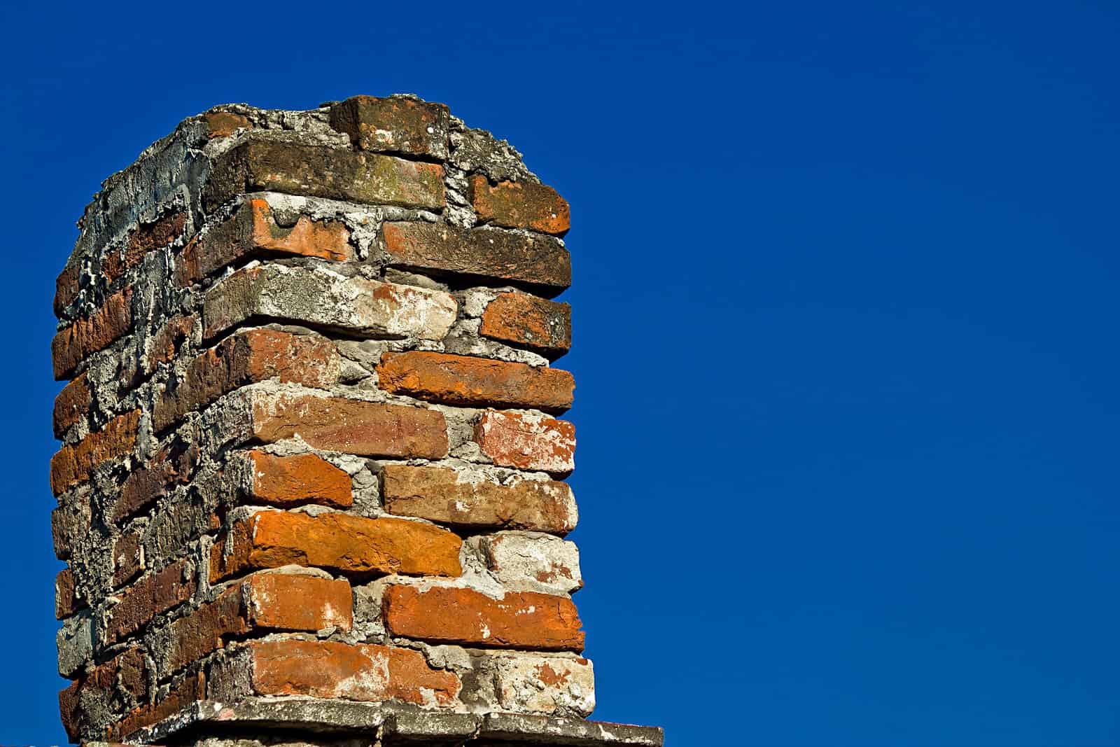 Close-up of an old brick chimney with weathered mortar against a clear blue sky.