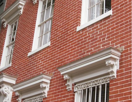 Close-up of historic brick masonry with decorative white window trims and ornate iron window guards.