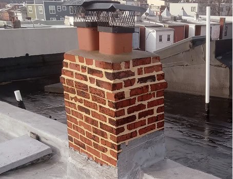 Chimney with brick masonry and tuckpointing on a rooftop.