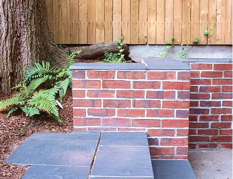 Close-up of historic brick masonry with tuckpointing work near a tree and wooden fence.