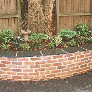 Close-up of a brick garden wall with detailed tuckpointing work and lush greenery.
