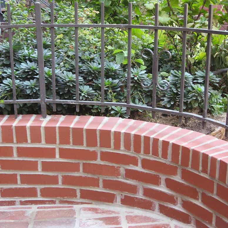 Close-up of brick masonry with decorative iron fence and lush greenery.