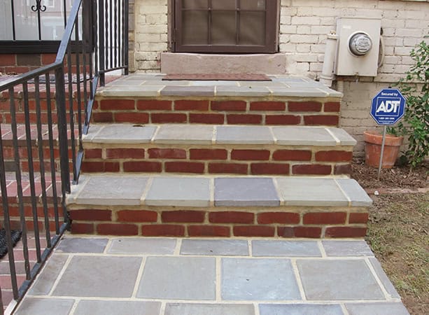 Brick and stone masonry steps leading to a residential door with security system sign.