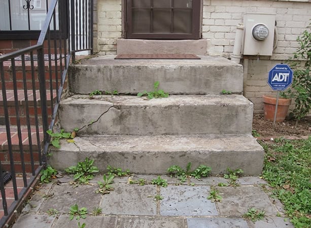 Cracked concrete stairs with weeds growing between the cracks in front of a brick building.